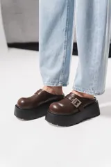 Zuecos de plataforma alta estilo chunky, color negro, con diseño destalonado y una tira en el empeine con hebilla metálica plateada.