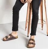 Sandalias Birkenstock modelo Arizona con diseño de dos correas ajustables. Confeccionadas en cuero nobuk aceitado, cuentan con plantilla anatómica Soft Footbed con capa de espuma adicional para mayor confort y suela resistente.