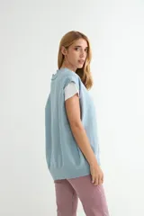 Chaleco de punto color verde, con escote en V y cierre frontal de botones negros. Presenta un diseño holgado con terminaciones acanaladas en el cuello, sisas y ruedo.