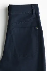 Pantalón acampanado de lona de algodón en color azul marino, con cintura de tiro alto, cierre de botón frontal y pliegues marcados en las piernas.