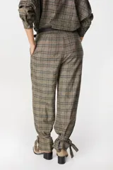 Pantalón de tiro medio con estampado a cuadros, corte holgado y pinzas en la cintura. Presenta un diseño distintivo con tiras ajustables en los tobillos que permiten crear un efecto fruncido.