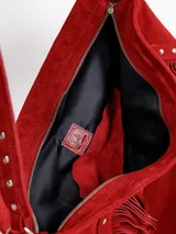Cartera tipo hobo color rojo, confeccionada en gamuza, con flecos laterales, tachas metálicas decorativas y asa de hombro.