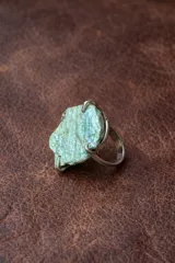 Anillo de alpaca con piedra natural de color verde azulado, de forma irregular y textura rugosa, sujetada por garras metálicas.