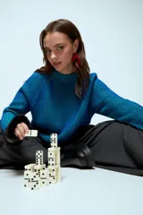 Sweater de punto con hilo de lurex brillante, color azul con rayas verticales en verde. Presenta cuello redondo, mangas largas con puños de piel sintética negra y corte holgado.