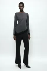 Top de manga larga en tejido de punto suave color gris, con cuello redondo y bajo asimétrico decorado con encaje negro a tono. Presenta detalles de encaje negro en los puños.