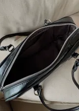 Cartera de hombro tipo baguette en color negro con acabado brillante efecto cuero arrugado. Presenta una estructura rectangular con bordes redondeados, cierre superior y doble asa fija.