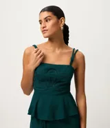 Blusa verde oscura de tirantes dobles con nudos, escote recto y corpiño estructurado con detalle de flor en relieve. Presenta un corte peplum en el bajo y espalda con nido de abejas.