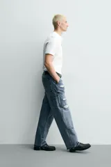 Pantalón de jean estilo carpintero con corte relaxed fit, tiro medio y pierna recta. Presenta un lavado azul medio con efecto desgastado y roturas en las rodillas. Incluye bolsillos laterales tipo plastrón, tira multifunción en la pierna, cierre frontal con cremallera y botón.