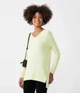 Blusa de punto color amarillo claro, con escote en V, mangas largas con textura acanalada y diseño de ruedo asimétrico tipo mullet con aberturas laterales.