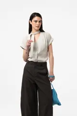 Camisa gris de corte relajado, con escote en V y lazo largo incorporado en el cuello. Mangas cortas con vuelta y frunce sutil en los hombros.