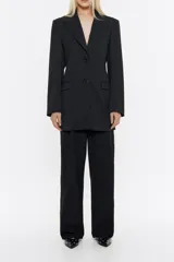 Chaqueta negra estilo sastre cruzada, de corte ajustado en cintura, con escote con solapas, manga larga y cierre frontal con botonadura. Incluye bolsillos con tapeta y abertura en la parte posterior.