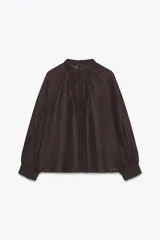 Blusa de cuello subido y manga larga abullonada con puños ajustados. Presenta un diseño semitransparente con textura arrugada y cierre frontal con botones a tono.