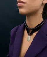 Collar tipo choker compuesto por una cinta de terciopelo color ciruela y una hilera de cuentas oscuras, con un dije colgante de piedra clara con un pequeño detalle incrustado.