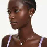 Conjunto de joyería compuesto por un collar y un par de aros de botón, ambos con diseño de flor. Cada pieza presenta una perla de cristal central rodeada de pétalos con pavé de cristales brillantes, con baño de rodio.