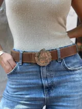 Cinturón de cuero marrón con hebilla metálica grande en forma de escudo nacional.