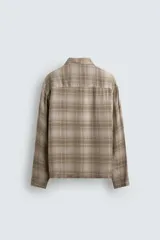 Camisa relaxed fit de manga larga con cuello solapa, confeccionada en tejido con mezcla de viscosa. Presenta un bolsillo plastrón en el pecho, bajo con aberturas laterales y cierre frontal de botonadura. El diseño es a cuadros en tonos beige y marrón.