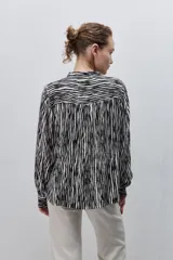 Camisa de calce amplio y fluido de viscosa liviana, con estampado de rayas verticales irregulares en blanco y negro, cuello mao, abotonadura frontal y mangas largas.