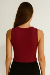 Top sin mangas color blanco hueso, de tejido acanalado, corte ajustado al cuerpo y cuello redondo con tres recortes en forma de ojo de cerradura en el centro del pecho.