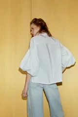 Camisa de algodón con cuello solapa y cierre frontal con botones ocultos. Presenta mangas abullonadas por debajo del codo con terminación elástica.