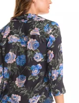 Camisa de gasa con estampado floral en tonos azules y rosados sobre fondo negro. Presenta cuello con solapa, escote en V, cierre frontal con botones y mangas tres cuartos con puños abotonados.