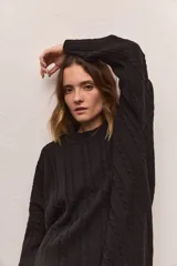 Buzo tejido ancho de algodón color negro, con cuello redondo y mangas largas. Presenta un diseño de trenzas verticales en el tejido.