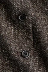 Chaleco largo de vestir, color marrón oscuro jaspeado, con cuello redondo, cierre frontal de botones y bolsillos ribeteados. Presenta un corte entallado y forro interior.