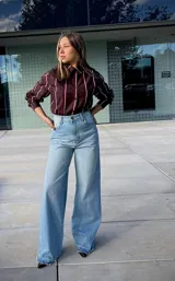 Jean de corte wide leg en color celeste claro, con tiro alto y ruedo deshilachado. Presenta un diseño de pierna ancha y cierre frontal con botón y cremallera.