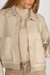 Sobrecamisa negra de paño con bordados geométricos en color crudo en el cuello, solapas, puños, bolsillos y bajo. Tiene cierre frontal con botones y bolsillos laterales.