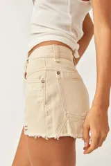 Short de denim color beige, de tiro medio y silueta relajada, con cinco bolsillos, cierre frontal con botón y cremallera, y detalles de roturas y bordes deshilachados.