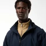 Chaqueta cortavientos azul marino con capucha, cierre frontal y bolsillos con solapa a la altura de la cintura. Presenta un diseño técnico y holgado.