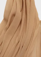 Vestido largo de gasa color tostado, con diseño recto y cuello halter cruzado con detalle drapeado. Presenta un diseño semitransparente con forro interior y cierre de cremallera en la parte posterior.