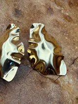 Aros dorados con diseño irregular y acabado brillante, que simulan la forma de una duna.