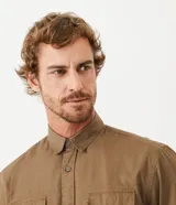 Camisa de manga larga confeccionada en sarga de algodón, con cuello clásico, cierre frontal abotonado y dos bolsillos frontales con solapa y botón.