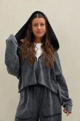 Campera crop estilo hoodie con capucha, cierre frontal completo y efecto acid wash en color negro, de mangas largas amplias y calce holgado.