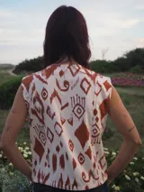 Chaleco de lino estampado con diseño ikat en tonos marrón y crudo, sin mangas, con cuello redondo y cierre frontal de botones tapados.