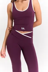 Conjunto deportivo compuesto por un top de escote redondo con ribetes blancos y una calza de tiro alto con cintura cruzada y detalle de ribete blanco. Ambas prendas son de color uva y cuentan con el logo bk. estampado en el top.