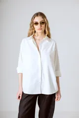 Camisa blanca de corte clásico, con cuello camisero y mangas largas con puños abotonados.