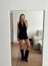 Vestido corto negro con escote halter profundo y diseño drapeado en la parte frontal y lateral. Confeccionado en tela elástica ajustada al cuerpo.