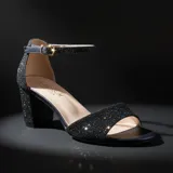 Sandalia de tacón cuadrado medio, con acabado brillante tipo glitter en color negro. Presenta una tira frontal abierta y una tira ajustable con hebilla metálica en el tobillo.