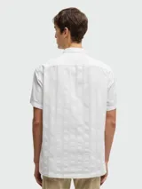 Camisa blanca de manga corta con cuello clásico y botones frontales. Presenta un tejido texturizado con finas rayas verticales en relieve.