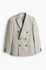 Blazer de doble botonadura en color beige, con solapas de pico, bolsillos delanteros con solapa y botones oscuros en contraste. Presenta un corte estándar con abertura doble en la parte trasera y forro interior.