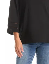 Blusa negra de silueta fluida con textura gofrada. Presenta cuello a la base y mangas tres cuartos acampanadas, ambos decorados con detalles de calados geométricos.