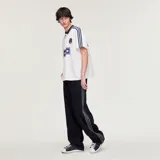 Camiseta Adidas Originals x Oasis de manga corta, color blanco con detalles en azul marino. Presenta cuello polo, las tres tiras características de la marca en los hombros, el logo del trifolio y un estampado frontal con la inscripción "oasis".
