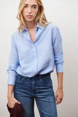 Camisa de mujer a rayas verticales blancas y rosadas, con cuello clásico, cierre de botones frontal y mangas largas con puños abotonados.