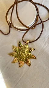 Colgante dorado con forma de sol de 8 puntas, con cordón negro.