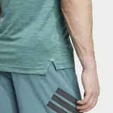 Remera de entrenamiento Adidas de corte ajustado, color verde jaspeado, con cuello redondo y mangas raglán. Presenta el logo de Adidas Badge of Sport en negro en el pecho.