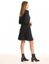 Vestido corto negro de crepe, con cuello solapa y escote en V. Presenta bolsillos simulados con cierres metálicos dorados en la parte delantera y mangas largas regulables con presilla y botón. La cintura es elastizada.