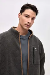 Campera de sherpa con textura capitoneada, color gris oscuro, con cierre frontal y detalles en color tostado. Cuenta con bolsillo en el pecho con cierre y bordado decorativo.