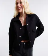 Campera corta negra de polivelour con cuello inglés, manga larga, cierre abotonado, bolsillos con solapa y botones en el pecho.