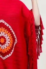 Poncho rojo de tejido artesanal con aplique central de crochet en forma de mandala con tonos amarillos, blancos y rojos. Presenta terminación con flecos en los laterales y diseño holgado.